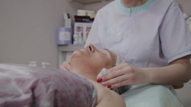 Güzellik uzmanı, bir kozmetoloji kliniğinde yaşlı bir kadının yüzünü yıkama işlemini gerçekleştirir.