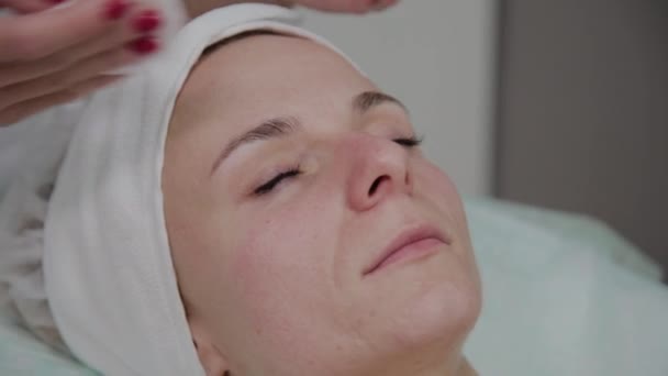 Una hermosa esteticista se frota la cara con una almohadilla de algodón antes del procedimiento . — Vídeos de Stock