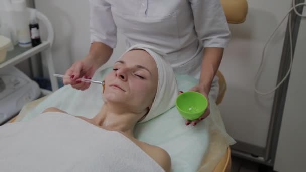 Cosmetologist profissional põe uma máscara na cara de pacientes . — Vídeo de Stock