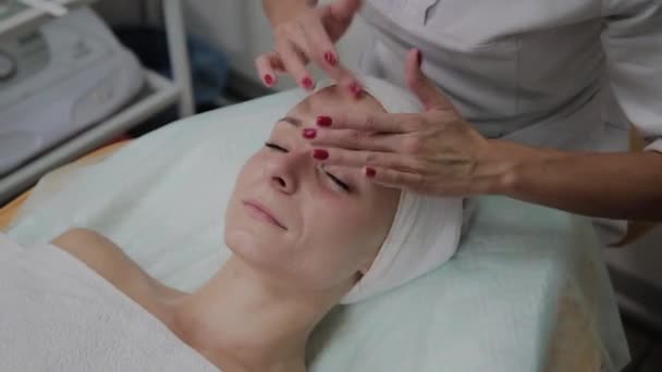 Профессиональный косметолог наносит увлажняющий крем на лицо девушки . — стоковое видео