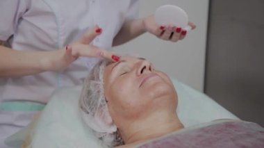 Profesyonel kozmetolojist güzellik salonunda yaşlı kadın için koruyucu krem uygular.
