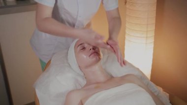Profesyonel kozmetolojist güzellik salonunda genç bir kızın vücuduna masaj kremi uygular.