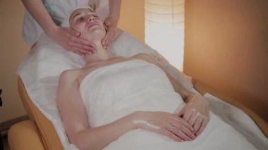 Profesyonel güzellik kozmetoloji ofisinde genç bir kız için karmaşık bir masaj yapar.