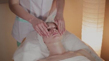 Profesyonel güzellik kozmetoloji ofisinde genç bir kız için karmaşık bir masaj yapar.