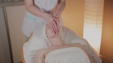 Profesyonel güzellik kozmetoloji ofisinde genç bir kız için karmaşık bir masaj yapar.
