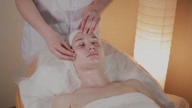 Profesyonel güzellik kozmetoloji ofisinde genç bir kız için karmaşık bir masaj yapar.