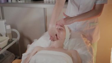 Profesyonel güzellik kozmetoloji ofisinde genç bir kız için karmaşık bir masaj yapar.
