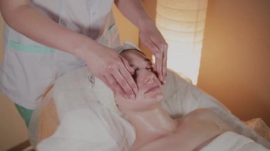Profesyonel güzellik kozmetoloji ofisinde genç bir kız için karmaşık bir masaj yapar.
