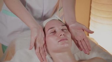 Profesyonel güzellik kozmetoloji ofisinde genç bir kız için karmaşık bir masaj yapar.