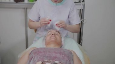 Güzellik uzmanı, bir kozmetoloji kliniğinde yaşlı bir kadının yüzünü yıkama işlemini gerçekleştirir.