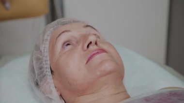 Güzellik uzmanı kozmetoloji kliniğinde yaşlı bir kadına makyaj kaldırır.