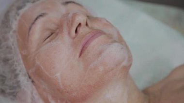 Yaşlı bir kadın kozmetoloji kliniğinde kanepede yatıyor..