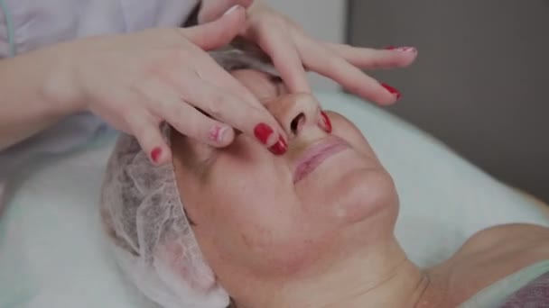 Femme cosmétologue faisant un massage du visage à une femme âgée dans une clinique cosmétologique . — Video