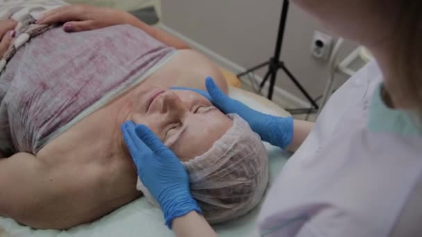 Kvinnlig kosmetolog gör ansiktsmassage till äldre kvinna i kosmetika klinik. — Stockvideo