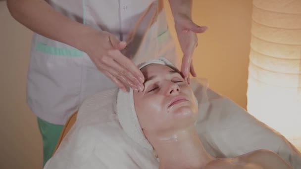 Esteticista profissional faz uma massagem complexa para uma jovem no escritório de cosmetologia . — Vídeo de Stock