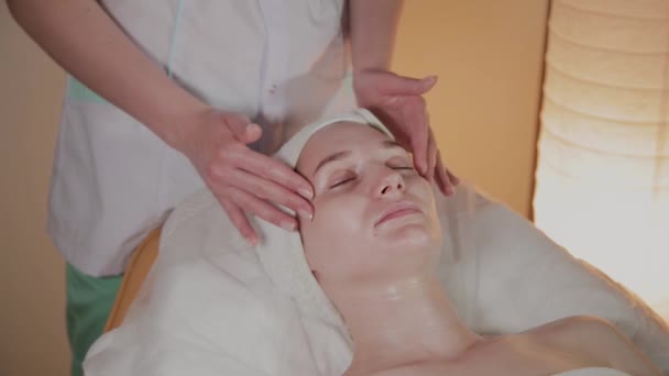 Профессиональный косметолог делает сложный массаж молодой девушке в косметологическом кабинете . — стоковое видео