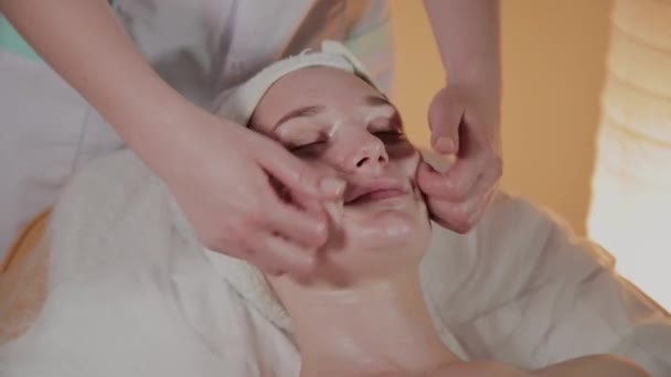 Esteticista profissional faz uma massagem complexa para uma jovem no escritório de cosmetologia . — Vídeo de Stock