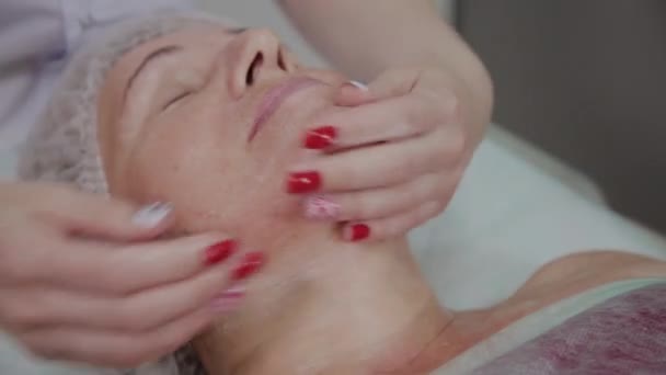 Cosmetóloga femenina haciendo masaje facial a anciana en clínica cosmetológica . — Vídeos de Stock