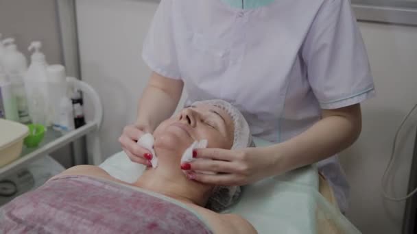 Güzellik uzmanı, bir kozmetoloji kliniğinde yaşlı bir kadının yüzünü yıkama işlemini gerçekleştirir. — Stok video