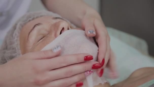 Професійний косметолог накладає серветки на обличчя літньої жінки в косметологічному кабінеті . — стокове відео