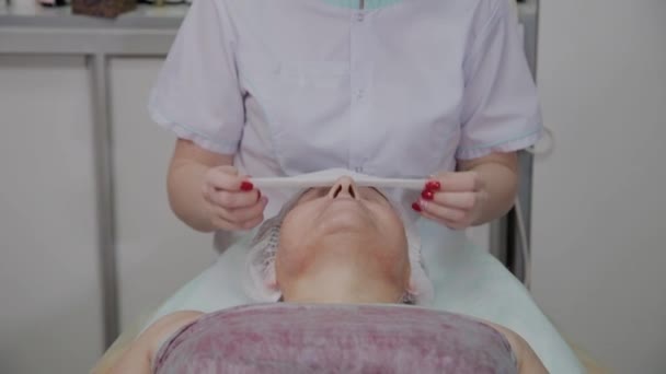 Esteticista profesional elimina las toallitas de la cara de una mujer mayor en la oficina de cosmetología . — Vídeo de stock