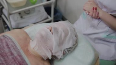 Güzellik salonunda yatan yaşlı bir kadının yüzündeki nemlendirici mendiller.