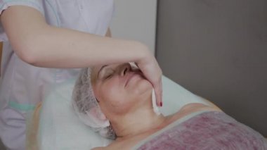 Güzellik uzmanı, bir kozmetoloji kliniğinde yaşlı bir kadının yüzünü yıkama işlemini gerçekleştirir.