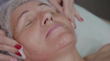 Güzellik uzmanı, bir kozmetoloji kliniğinde yaşlı bir kadının yüzünü yıkama işlemini gerçekleştirir.