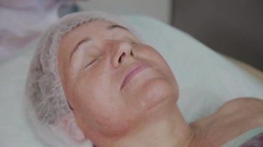 Yaşlı bir kadın kozmetoloji kliniğinde kanepede yatıyor..