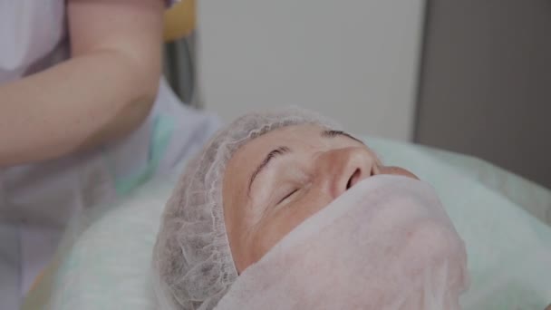 Esteticista profissional impõe toalhetes no rosto de uma mulher idosa no escritório de cosmetologia . — Vídeo de Stock