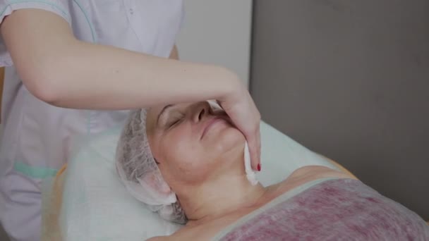 Esteticista realiza el procedimiento de lavado de la cara de una mujer mayor en una clínica de cosmetología . — Vídeos de Stock