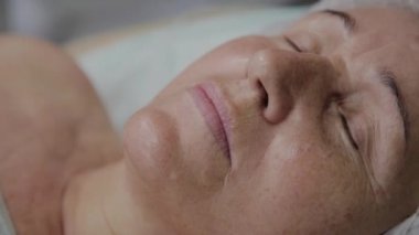 Yaşlı bir kadın kozmetoloji kliniğinde kanepede yatıyor..