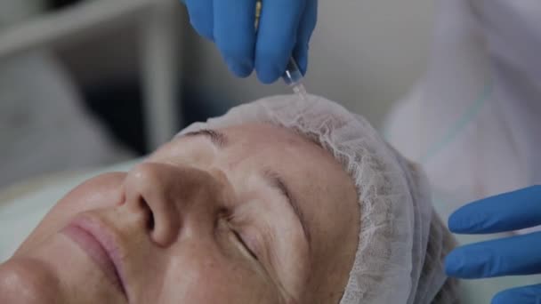 Cosmetólogo profesional aplica suero a la cara de una anciana en el salón de belleza . — Vídeos de Stock