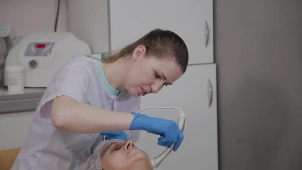 Профессиональный косметолог проводит процедуру для пожилой женщины с микротоками в отделении косметологии . — стоковое видео