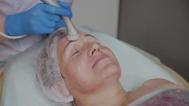 Cosmetologist profissional executa o procedimento para uma mulher idosa com microcorrentes no escritório de cosmetologia . — Vídeo de Stock