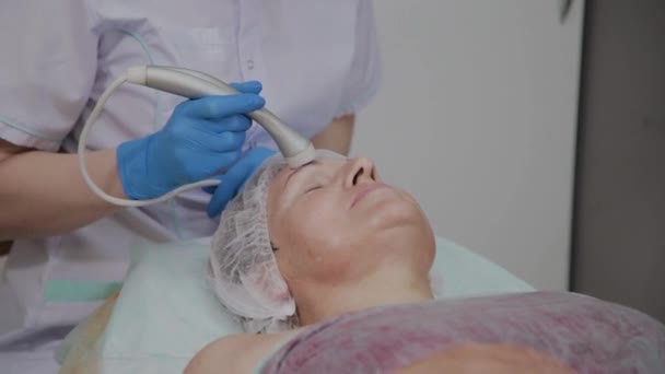 Cosmetologist profissional executa o procedimento para uma mulher idosa com microcorrentes no escritório de cosmetologia . — Vídeo de Stock