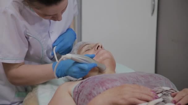 Professionele cosmetoloog voert de procedure voor een oudere vrouw met micro stromingen in het cosmetologie kantoor. — Stockvideo