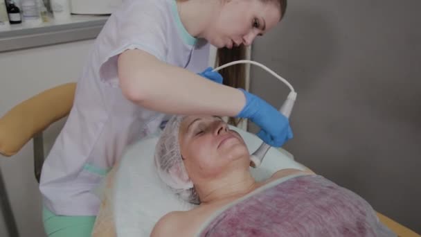 Профессиональный косметолог проводит процедуру для пожилой женщины с микротоками в отделении косметологии . — стоковое видео