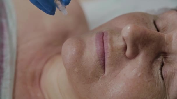 Профессиональный косметолог наносит сыворотку на лицо пожилой женщины в салоне красоты . — стоковое видео