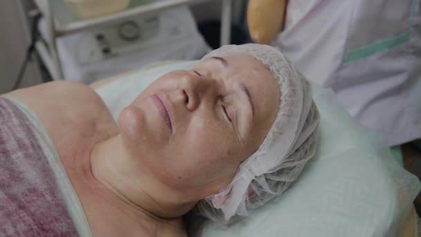 Uma mulher idosa está deitada em um sofá em uma clínica de cosmetologia . — Vídeo de Stock