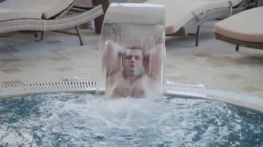 Neşeli adam bir şelalealtında yüzer ve havuzda poz.