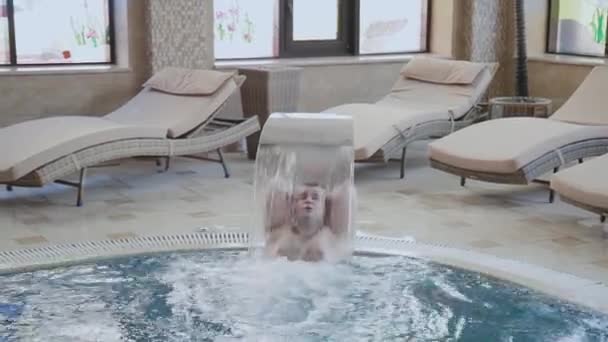 Fröhlicher Mann schwimmt unter einem Wasserfall und posiert im Pool. — Stockvideo