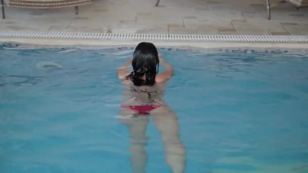 Mooi meisje zwemt naar de rand van het zwembad. — Stockvideo