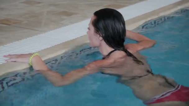 Una bella ragazza nuota fino al bordo della piscina e ne esce . — Video Stock