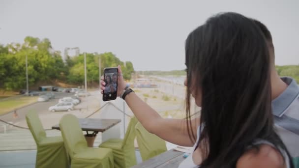 Een mooie vrouw en een vrolijke man nemen een selfie op de veranda van het restaurant. — Stockvideo