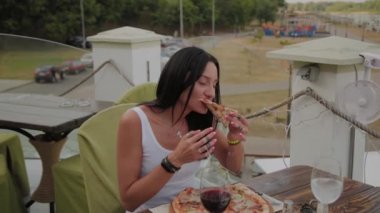 Bir restoranın terasında pizza yiyen güzel kadın.
