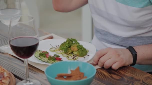 Een jongeman is lunchen met een salade met groenten in een restaurant op het open terras. Gezonde voeding. — Stockvideo