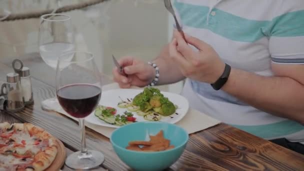 Un joven está almorzando con una ensalada con verduras en un restaurante en la terraza abierta. Alimento saludable . — Vídeos de Stock