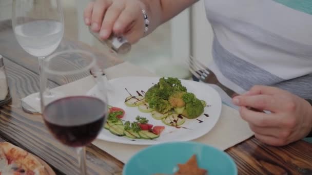 Een jongeman is lunchen met een salade met groenten in een restaurant op het open terras. Gezonde voeding. — Stockvideo