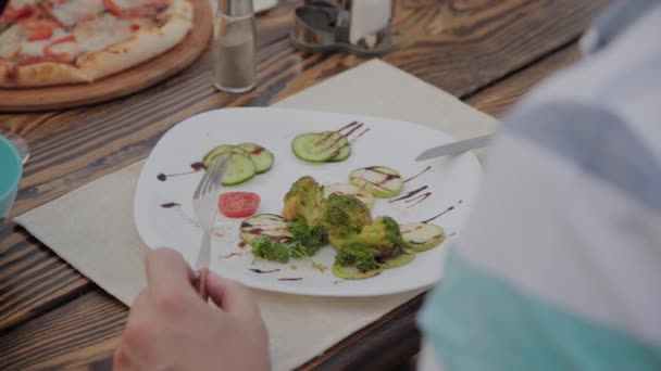 Genç bir adam açık terasta bir restoranda sebze li salata ile öğle yemeği yiyor. Sağlıklı gıda. — Stok video